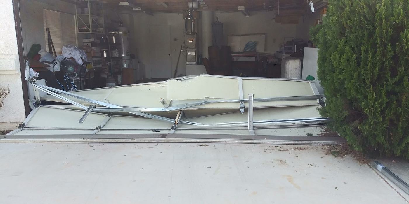 Garage door collapsed into the opening with buckled panels and twisted struts