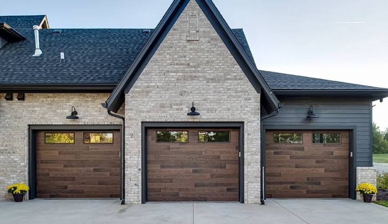 Three dark stained plank garage doors with glazed top rows on a brick elevation