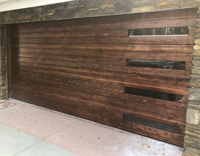 Dark walnut horizontal plank garage door with staggered glazing and a stone surround, installed by Classic Garage Doors in Riverside County
