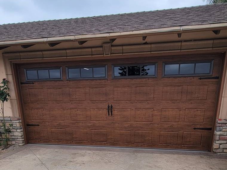 Walnut wood-grain steel garage door with a row of windows and strap hardware — installed and serviced by Riverside Classic Garage Doors across Riverside County, California