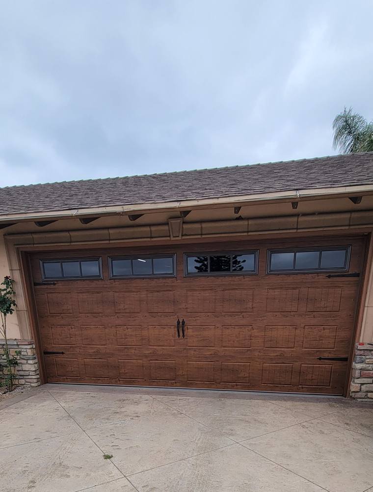 Walnut wood-grain steel garage door with window row and black strap hardware